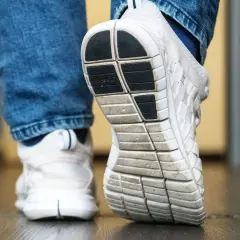 Nahaufnahme von weißen Turnschuhen mit Jeans. Die Sohle eines Schuhs ist deutlich zu sehen, bereit für den nächsten Schritt, der vielleicht quietschende Schuhe hinterlässt.