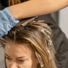 Manos enguantadas aplican mechas con papel de aluminio para un look face framing.