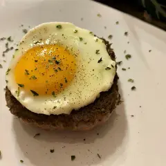 Un délicieux steak a cheval, un steak haché surmonté d'un œuf au plat, saupoudré d'herbes et de poivre.