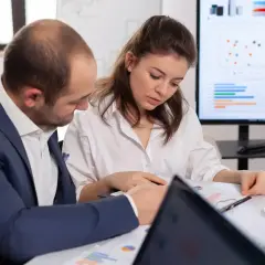 Przedstawiciel handlowy i jego koleżanka analizują wykresy na ekranie i dokumenty na stole.