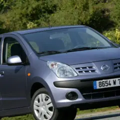 Niebieski Nissan Pixo z tablicą rejestracyjną 8654 W 78 zaparkowany na tle zieleni.