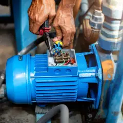 Manos trabajando en la caja de conexiones de un motor azul, revisando el cableado. El **vac significado** es crucial para el funcionamiento de esta bomba.