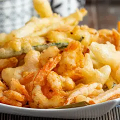 Un piatto invitante di gamberi in tempura dorati e croccanti, accompagnati da verdure fritte.