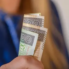 Orzeczenie o niepełnosprawności to podstawa do ubiegania się o zasiłek pielęgnacyjny. Dłonie trzymają banknoty 100 zł.