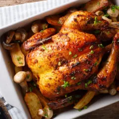 Un délicieux poulet au four, doré et croustillant, servi avec des pommes de terre rôties et des champignons.