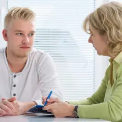Młody mężczyzna rozmawia z terapeutką, która notuje coś na kartce.