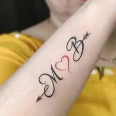 Tatuaż serce z inicjałami M i B, połączone strzałą. Symbol miłości i więzi.