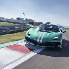 Zielony Ferrari 296 GTB z białymi pasami pędzi po torze wyścigowym, zostawiając za sobą rozmyte tło.