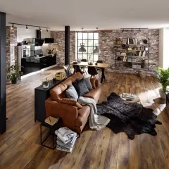 Geräumiges Wohnzimmer im industrial style mit brauner Ledercouch, Holztisch und Ziegelwand.