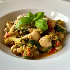 Pyszne kaszotto z warzywami: brokuły, cukinia, pieczarki i pomidorki, posypane parmezanem i udekorowane bazylią.
