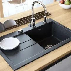 Nowoczesny blat kuchenny z drewnianym wykończeniem, na którym znajduje się czarny zlew granitowy. Pokazano, jak wyciąć otwór w blacie pod zlew granitowy, z widocznym kranem i dozownikiem mydła.