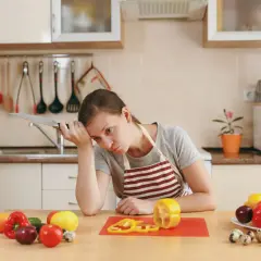 Zmęczona kobieta z nożem w dłoni zastanawia się, czy dieta pudełkowa się opłaca. Na stole warzywa i jajka.