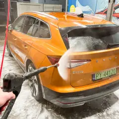 Pomarańczowy Skoda Enyaq jest myty na myjni bezdotykowej. Woda pod ciśnieniem spływa po karoserii, tworząc pianę.