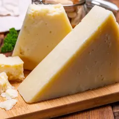 Fette di pecorino stagionato su tagliere di legno, con briciole e grissini sullo sfondo.