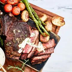 En saftig tomahawk-biff, perfekt grillad, serveras med rostade tomater, sparris och potatis. En krämig sås fulländar denna grillupplevelse.