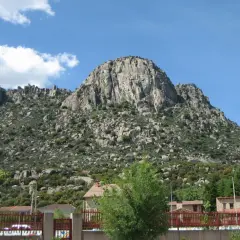Majestuosa sierra de la Cabrera, con sus rocas imponentes y vegetación verde, bajo un cielo azul con nubes blancas.