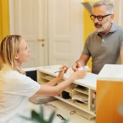 Uśmiechnięta rejestratorka medyczna podaje pacjentowi dokumenty.