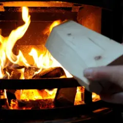 Holzscheit wird in einen brennenden Kamin gelegt. Vorsicht, keine Spanplatten verbrennen!