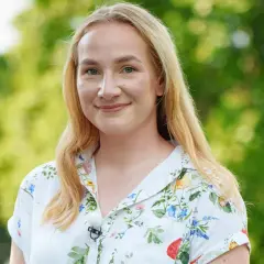 Uśmiechnięta Klaudia, uczestniczka "Rolnik szuka żony", w kwiecistej koszuli na tle zieleni.