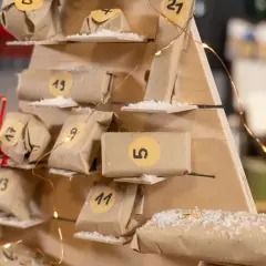 Drewniany kalendarz adwentowy dla dziecka diy, ozdobiony światełkami i małymi paczuszkami z numerami.