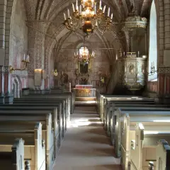 Interiör av en kyrka med bänkar, altare och en predikstol. Väggmålningar och en stor ljuskrona skapar en historisk atmosfär. En av många vackra kyrkor i Stockholm.