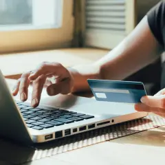 Person tippt auf Laptop, hält Visa-Karte. Prüft auf unberechtigte Abbuchung.