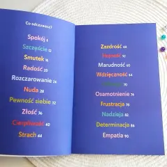 Otwarta książka z listą emocji: Spokój, Szczęście, Smutek, Radość, Rozczarowanie, Nuda, Pewność siebie, Złość, Cierpliwość, Strach, Zazdrość, Hojność, Marudność, Wdzięczność, Odwaga, Osamotnienie, Frustracja, Nadzieja, Determinacja, Empatia. To jakby z...