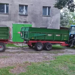 Ciągnik rolniczy z przyczepą, gotowy do pracy w kategorii B+E. Zielone przyczepy czekają na załadunek.