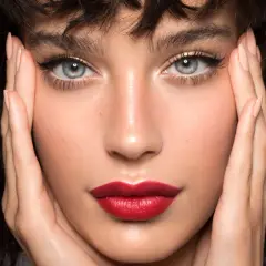 Close-up of a woman's face with perfect winged eyeliner and red lipstick, hands framing her face.