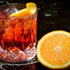 Ein erfrischender Negroni mit Eis und Orangenzeste, daneben eine saftige Orangenscheibe – die perfekten Negroni Zutaten.
