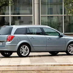 Srebrny Opel Astra H kombi zaparkowany przed nowoczesnym budynkiem z dużymi oknami.