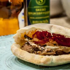 En saftig pulled pork karre-macka i pitabröd, fylld med krispig kål och rödlök. En öl i bakgrunden.