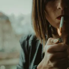 Kobieta zapala papierosa zapalniczką. Czy jest zakaz palenia papierosów na balkonie?