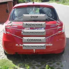Czerwony Suzuki Swift z oznaczeniami: STOP, POZYCYJNE, KIERUNKOWSKAZY, COFANIA, PRZECIWMGŁOWE. Pomoc w nauce rodzajów świateł w samochodzie egzamin.