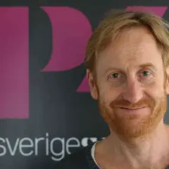 Gustaf Hammarsten, känd från filmer och tv-program, ler mot kameran framför en bakgrund med logotypen för Sveriges Television.