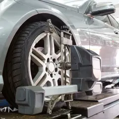 Un coche plateado en un elevador, con un dispositivo de alineación de ruedas fijado a la llanta delantera.