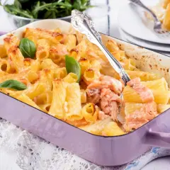 Zapiekanka z makaronem i łososiem w fioletowym naczyniu, udekorowana bazylią.