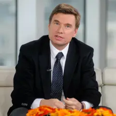 Jerzy Hubert Tyszkiewicz w garniturze i krawacie, siedzący na kanapie, udziela wywiadu.