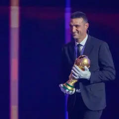 Uśmiechnięty trener Argentyny, Lionel Scaloni, trzyma Puchar Świata w złotych rękawiczkach.