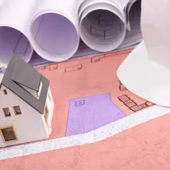 Model domu na planach, biały kask budowlany i zwoje projektów. Planowanie inwestycji, uwzględniające służebność przesyłu.