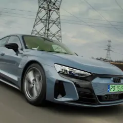 Szary, sportowy Audi GT jedzie po drodze, a w tle widać linie energetyczne i słupy.