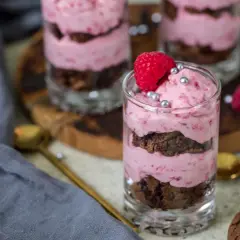 Ljuvlig hallonmousse till tårta i glas, varvad med chokladkaka och toppad med färsk hallon och silverkulor.