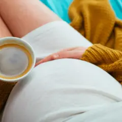 Una donna incinta si gode un caffè, con la mano che accarezza il pancione. Un momento di relax e dolce attesa.