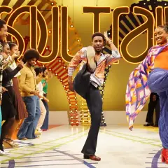 Ballerini in abiti colorati danzano sul palco di Soul Train, con un uomo che fa un calcio in aria e una donna che volteggia con uno scialle.