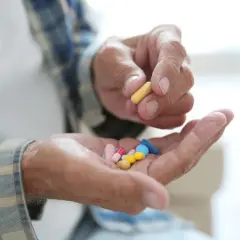 Dłoń starszego mężczyzny trzyma garść kolorowych tabletek, jedną żółtą kapsułkę, być może inhibitory MAO.
