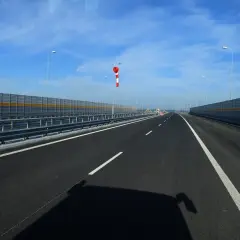 Pusta droga jednojezdniowa dwukierunkowa z barierami dźwiękochłonnymi i wiatrowskazem.