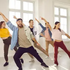 Grupa młodych ludzi wykonuje energiczne ruchy taneczne w jasnej sali.