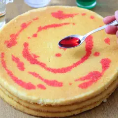 Un cucchiaino di sciroppo rosso viene versato su un pan di spagna a strati, creando un disegno.