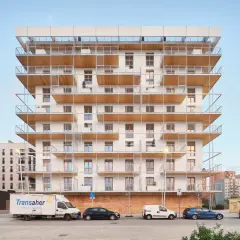 Edificio moderno con balcones de madera y metal. Posiblemente pisos de protección oficial en Barcelona, La Caixa, con vehículos aparcados.