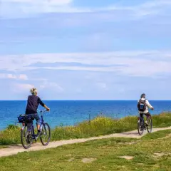 Dwie osoby jadą rowerami po malowniczej nadmorskiej trasie rowerowej. Piękne błękitne niebo i morze.